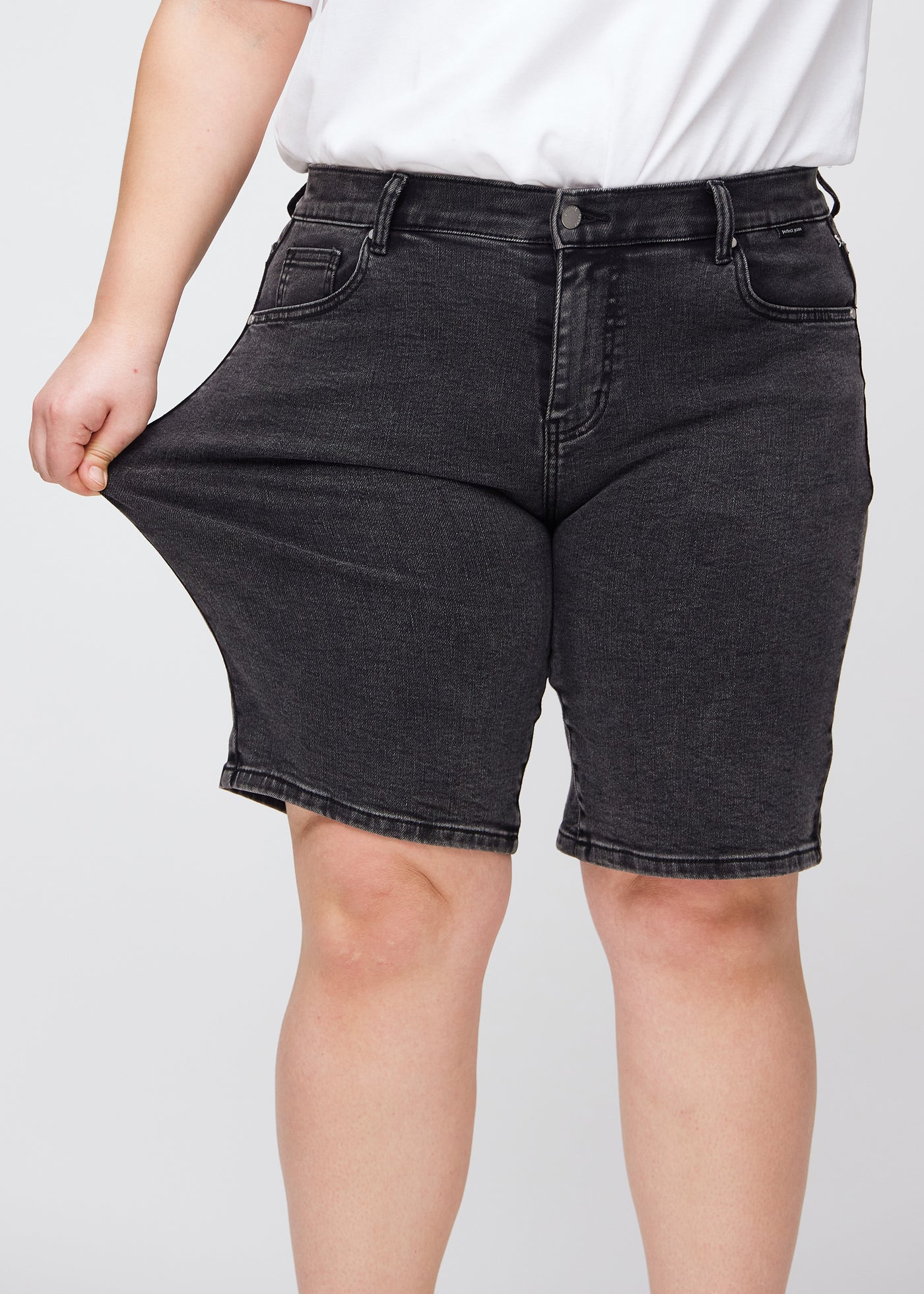 Plus-size model strækker shortsene ved låret for at vise stretch.