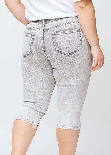 Tæt billede af bagdelen på en plus-size model i lysegrå denim slim capris – detaljefokus på lommer og syninger.