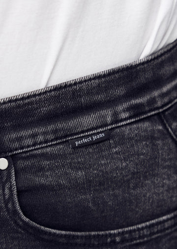 Nærbillede af mørkegrå denim med Perfect Jeans logoetiket ved forlommekanten.