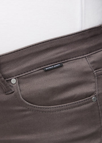 Nærbillede af gråbrunt jeansmateriale med Perfect Jeans logoetiket ved forlommekanten, på en plus-size model.