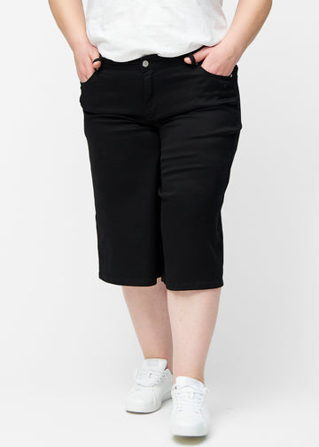Løse, sorte capris i farven Ravens set forfra på plus-size model, der sidder til ved hoften og falder løst ned.