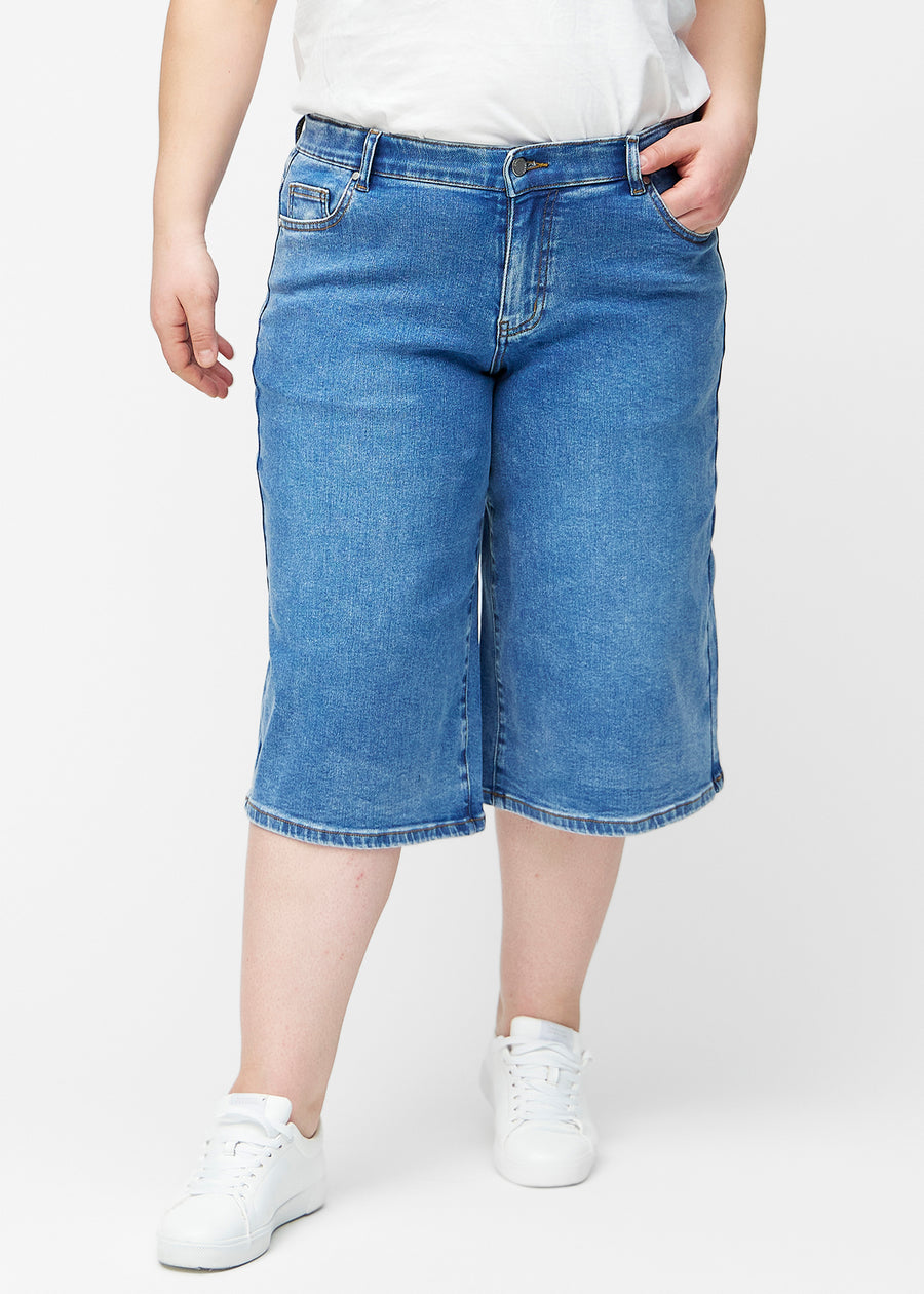 Løse, klassisk blå denim capris i farven Rivers set forfra på plus-size model, der sidder til ved hoften og falder løst ned.