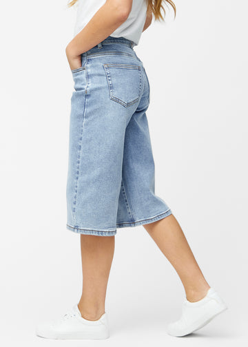 Loose, light blue denim capris in the colour Waves seen from the side on a model, where the wide fit and length to just below the knee are visible.
