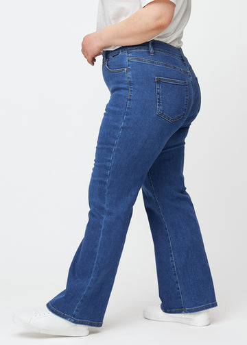 Mørkeblå mid-rise bootcut jeans i denimfarven Oceans set fra siden på en plus-size model.