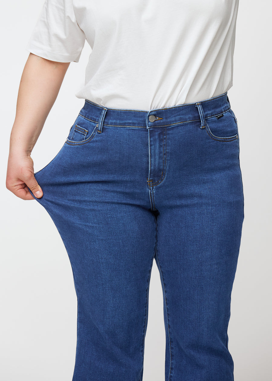 Plus-size model strækker jeansene ved låret for at vise stretch.