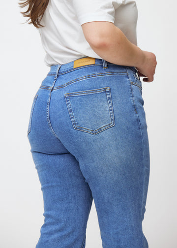 Blå mid-rise bootcut jeans i denimfarven Rivers set bagfra tæt på en plus-size model for at vise detaljer.