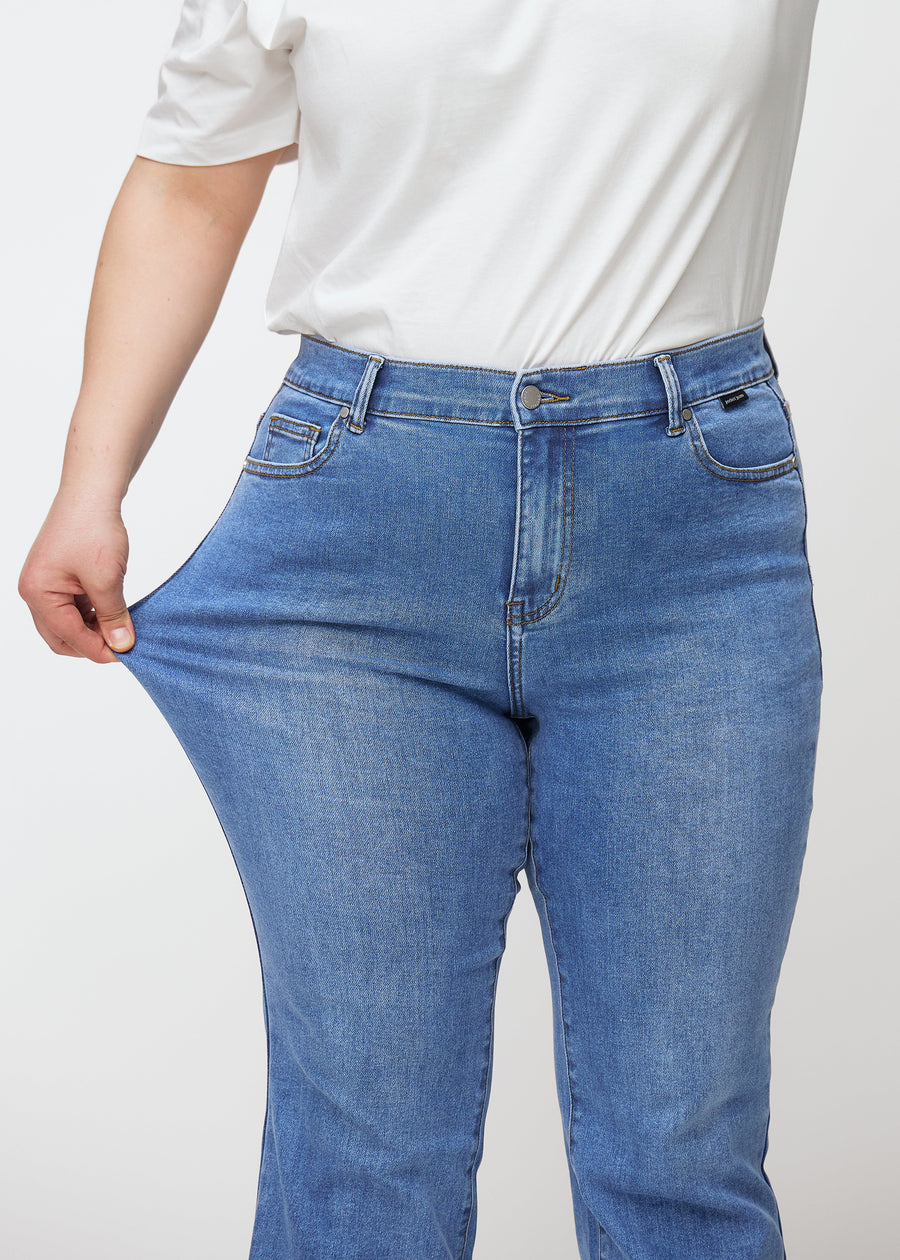 Plus-size model strækker jeansene ved låret for at vise stretch.