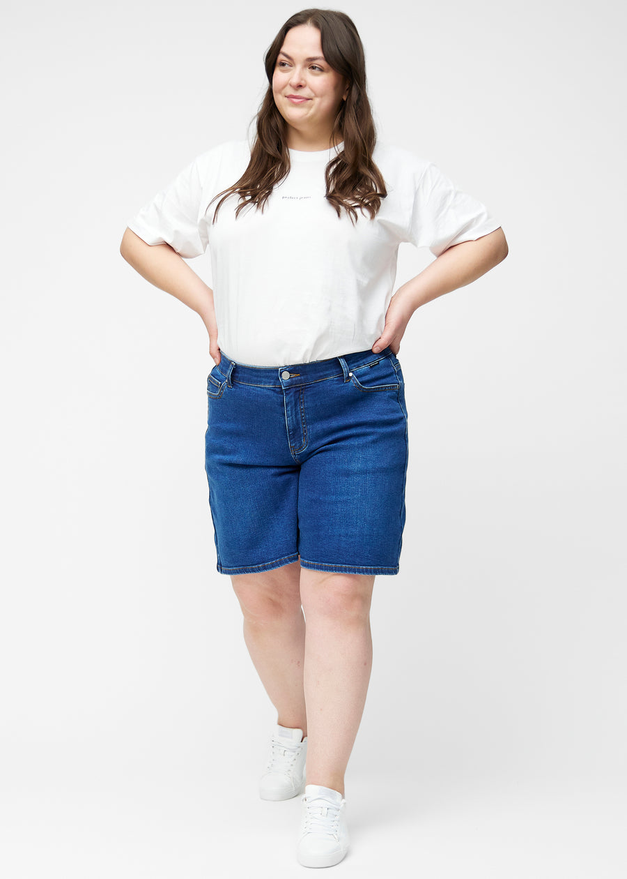 Fuldt billede af plus-size model i løse, mørkeblå denim shorts i farven Oceans, der går til lige over knæet.