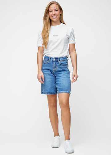 Fuldt billede af model i løse, klassisk blå denim shorts i farven Rivers, der går til lige over knæet.