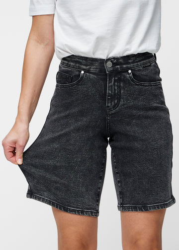 Model strækker de løse, mørkegrå denim shorts i farven Shadows ved hoften for at vise materialets stretch.