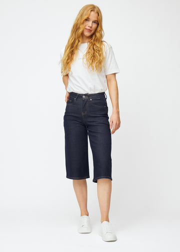 Full image of a model wearing deep dark blue denim capris for women in the colour Midnights with a loose fit.