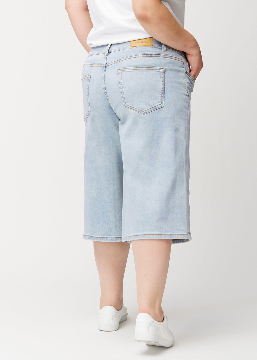 Back view of a plus-size model wearing loose, light blue Waves denim capris, showing the fit and length.
