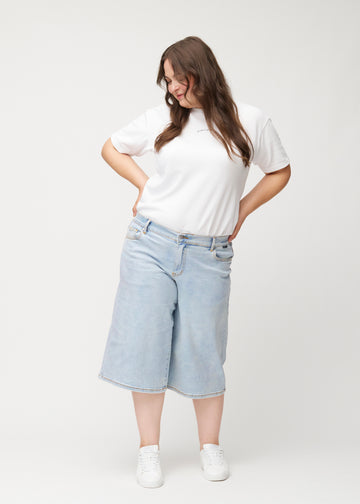 Full-length view of a plus-size model wearing loose, light blue Waves denim capris that end just below the knee.
