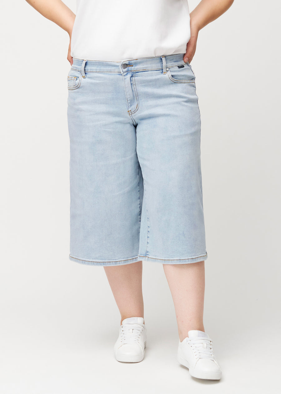 Front view of a plus-size model wearing loose, light blue Waves denim capris that fit at the hips and fall loosely.