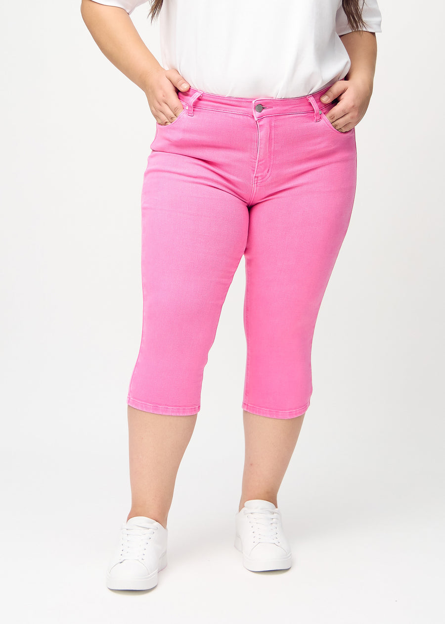 Skinny capris for women in pastel pink fabric, color Flamingos. Front view on a plus-size model, showing the close-fitting legs ending just below the knee.