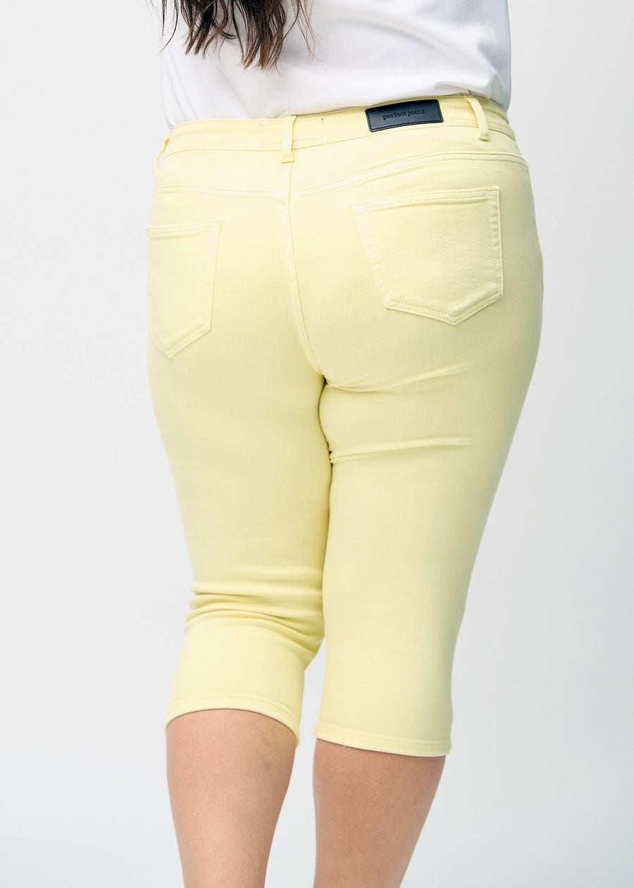 Skinny capris for women in pastel yellow fabric, color Lemonades. Close-up from behind on a plus-size model, highlighting pockets and stitching.