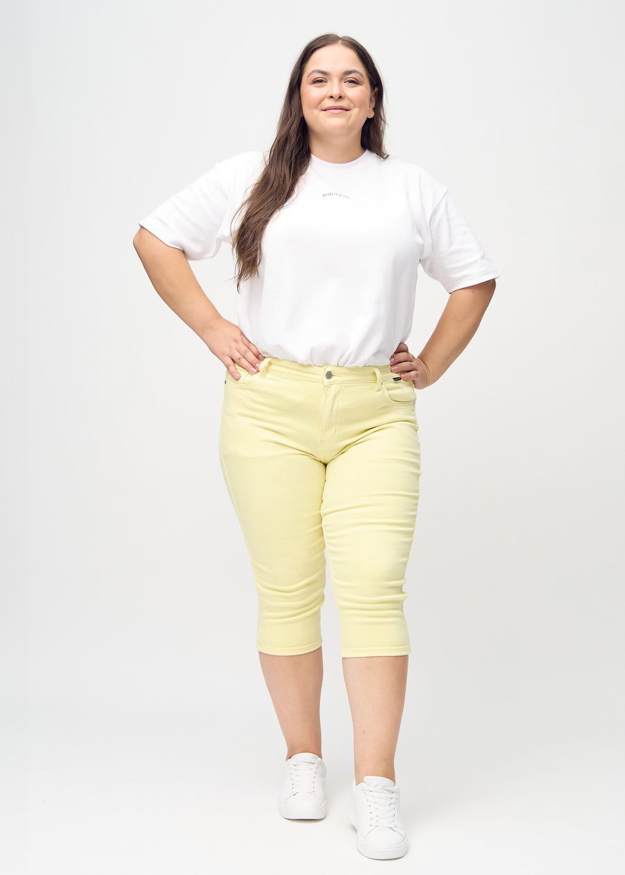 Skinny capris for women in pastel yellow fabric, color Lemonades. Full-length view of a plus-size model wearing the capris.