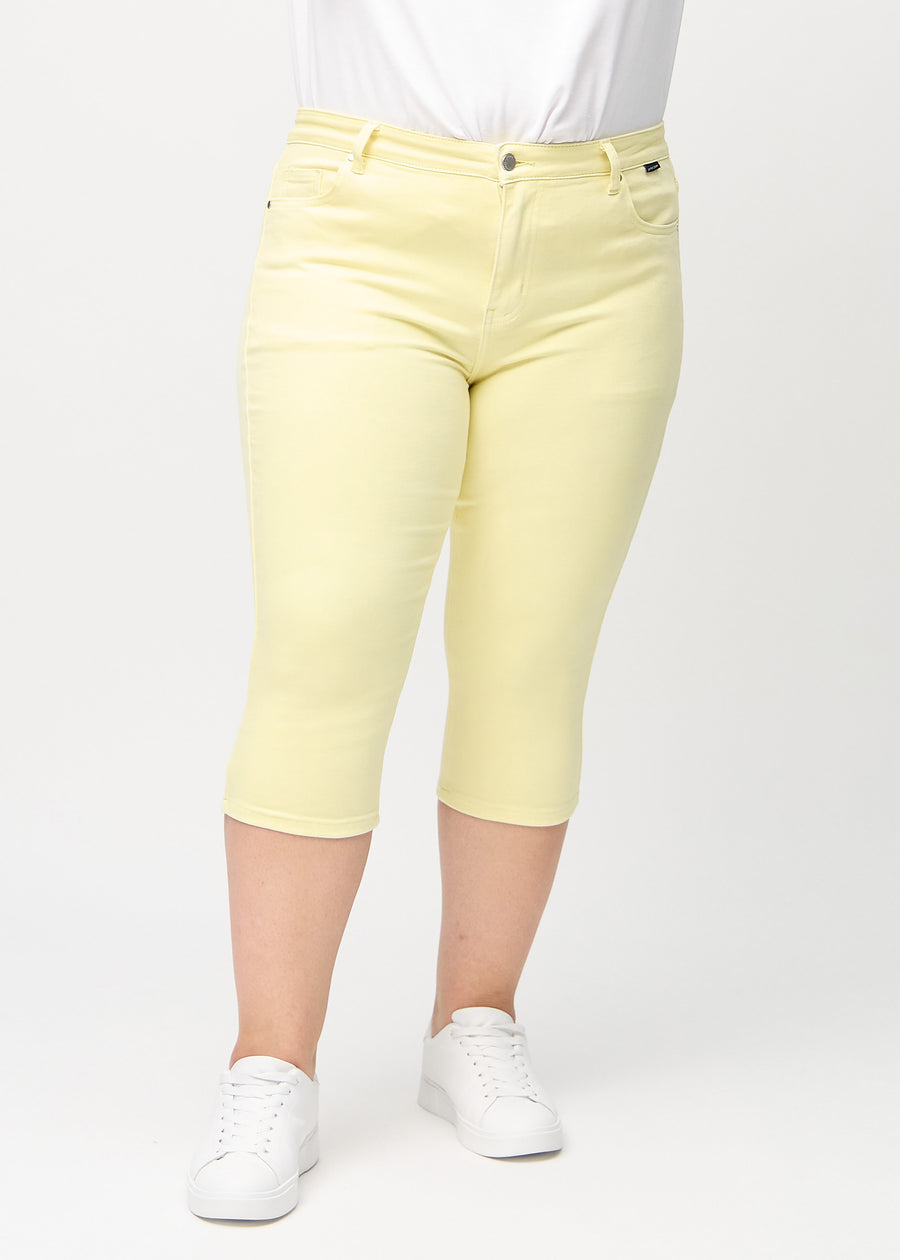 Skinny capris for women in pastel yellow fabric, color Lemonades. Front view on a plus-size model, showing the close-fitting legs ending just below the knee.