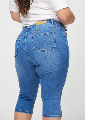 Skinny capris for women in blue denim, color Rivers. Close-up from behind on a plus-size model, highlighting pockets and stitching.