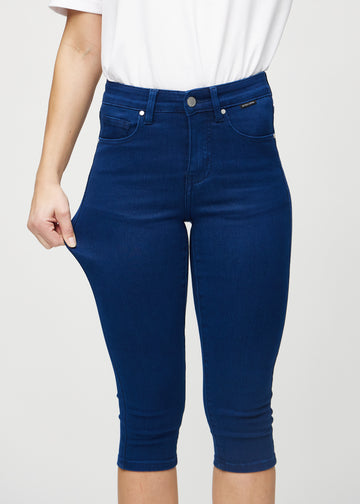 Skinny capris for women in dark blue fabric, color Royals. A model stretches the fabric to demonstrate its flexibility.