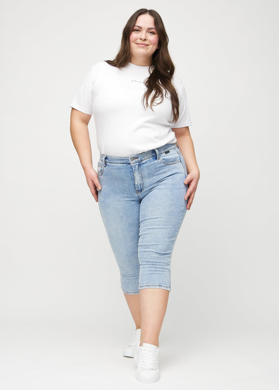 Skinny capris for women in light blue denim, color Waves. Full-length view of a plus-size model wearing the capris.