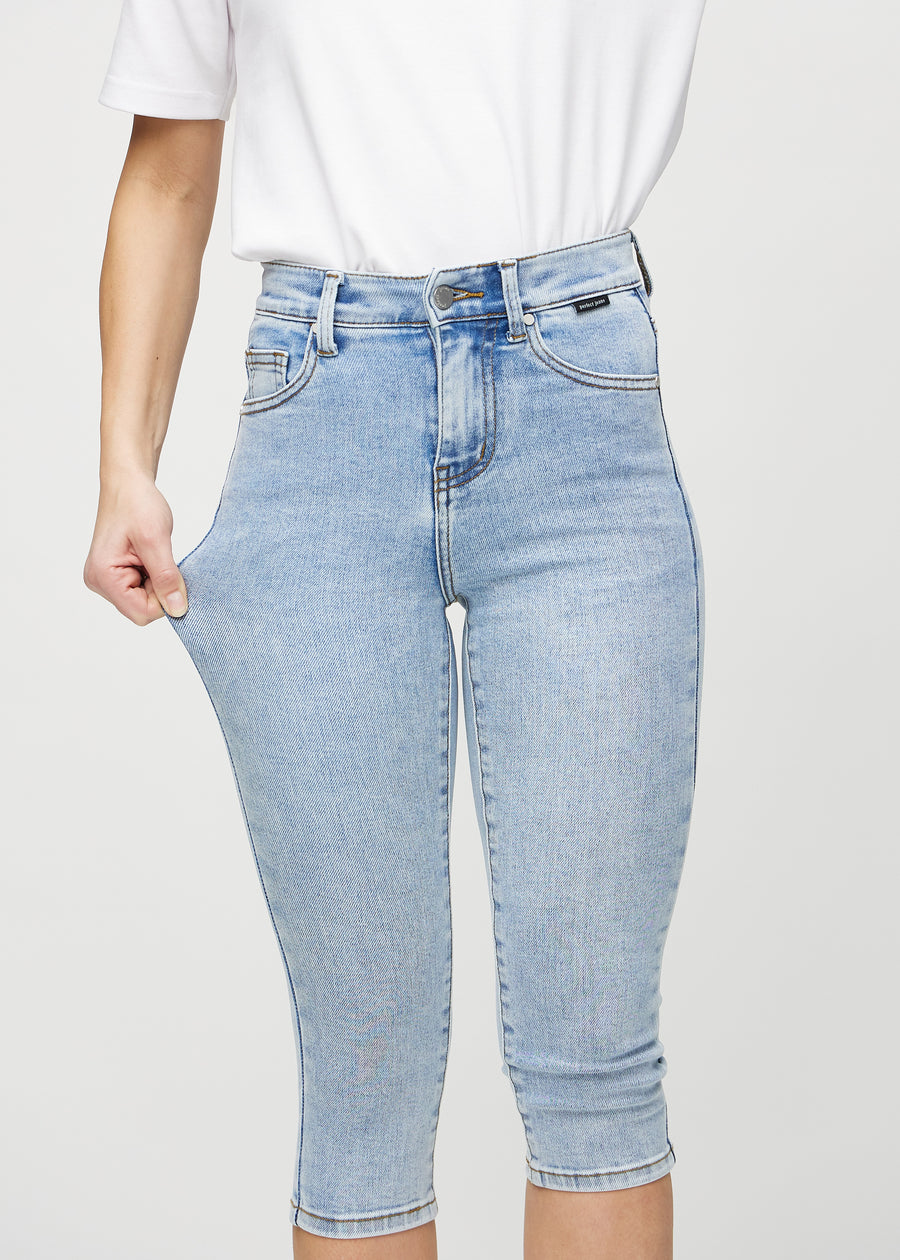 Skinny capris for women in light blue denim, color Waves. A model stretches the fabric to demonstrate its flexibility.