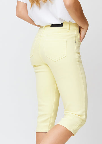 Slim capris for women in pastel light yellow jeans fabric, color Lemonades. Close-up from behind on a model, highlighting the back pockets and stitching.