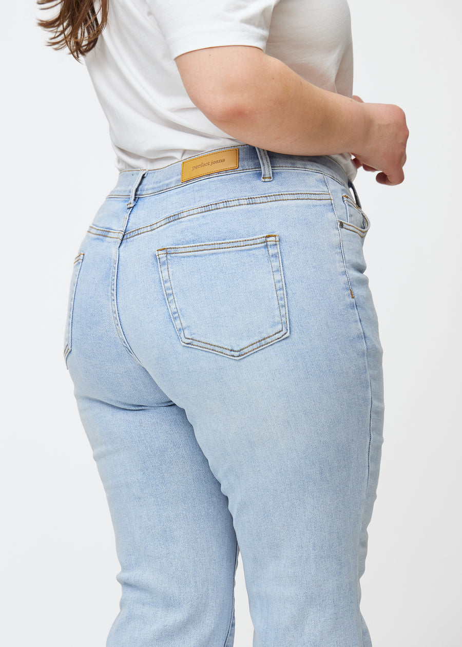 Light blue mid-rise bootcut jeans in Waves. Close-up back view on a plus-size model, showing the details.
