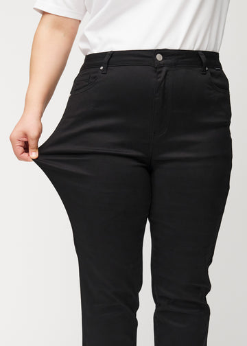 The plus-size model stretches the jeans at the thigh to show the stretch.