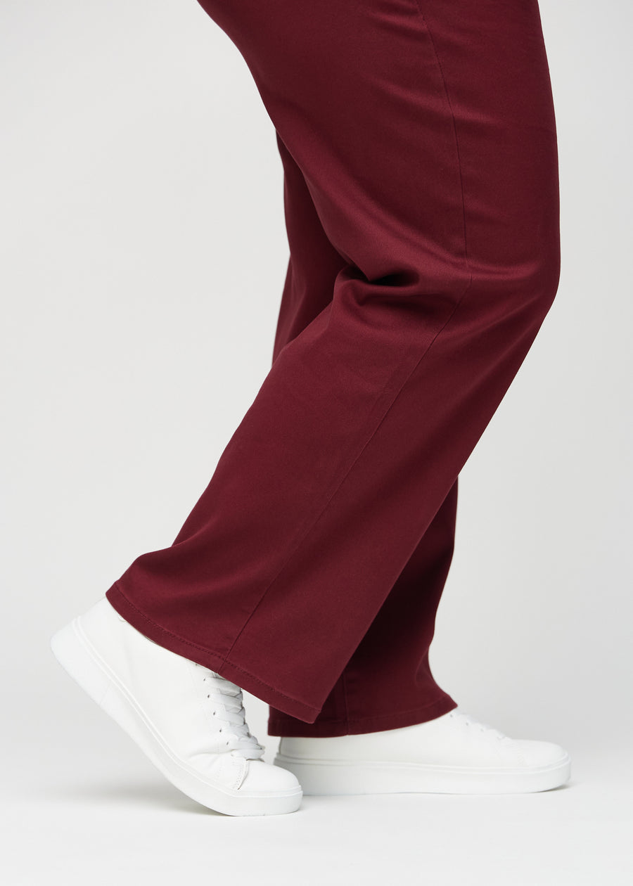 Loose jeans for women in dark red, color Santas. Close-up at the ankles on a plus-size model, showing the wide leg openings.