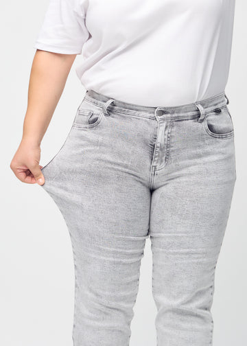 Regular jeans for women in light grey, color Ashes. A plus-size model stretches the fabric at the thigh to show its stretch.