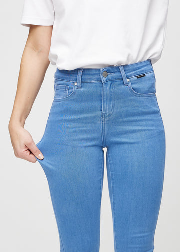 Skinny jeans for women in blue, color Geraniums. A model stretches the jeans at the thigh to show the fabric&