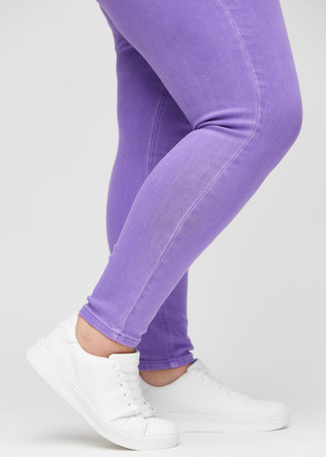 Skinny jeans for women in purple, color Lavenders. Close-up of the snug-fitting leg openings at the ankles on a plus-size model.