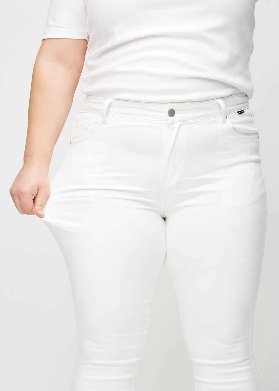 Skinny jeans for women in white, color Marguerites. A plus-size model stretches the jeans at the thigh to show the fabric&