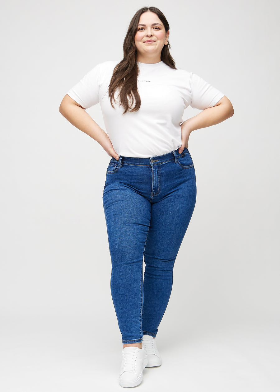 Skinny jeans for women in dark blue, color Oceans. Full-length view of a plus-size model in the jeans.
