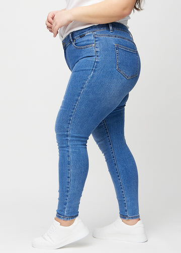 Skinny jeans for women in blue, color Rivers. Side view on a plus-size model.