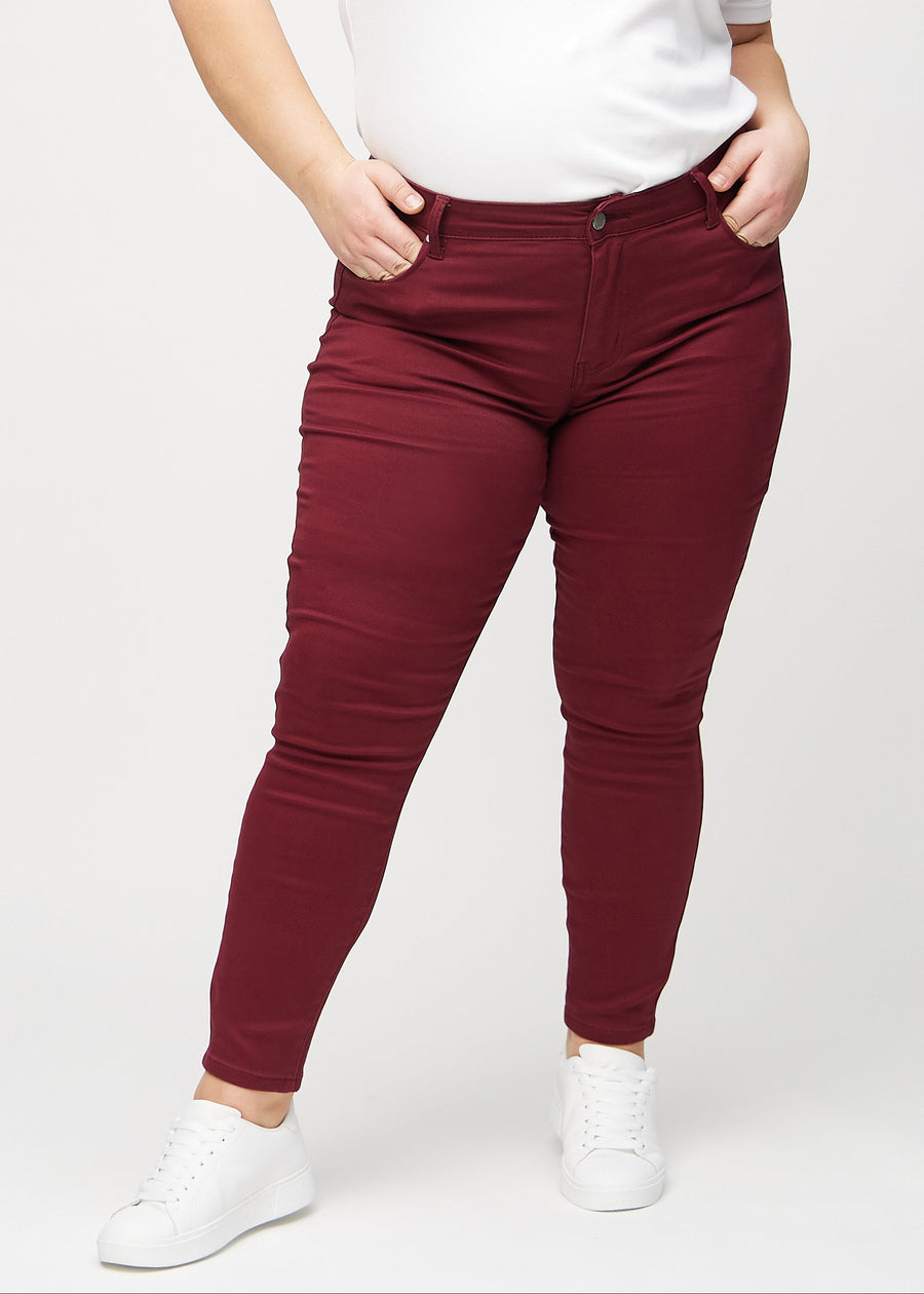 Skinny jeans for women in dark red, color Santas. Front view on a plus-size model, showing the close fit through the legs.
