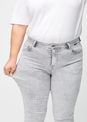 Slim jeans for women in light grey, color Ashes. A plus-size model stretches the jeans at the thigh to show the fabric&