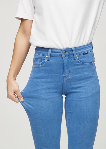 Slim jeans for women in blue, color Geraniums. A model stretches the jeans at the thigh to show the fabric&