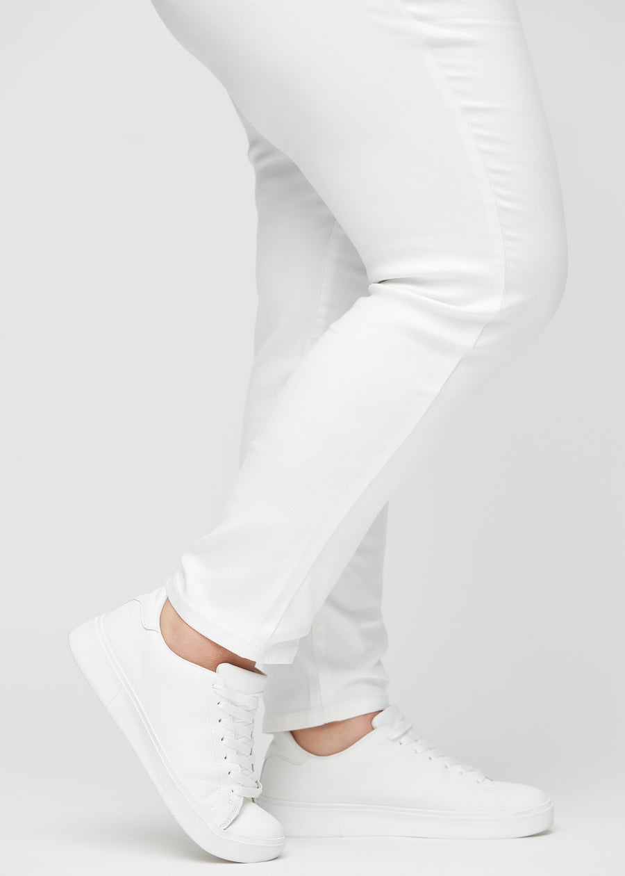 Slim jeans for women in white, color Marguerites. Close-up at the ankles on a plus-size model, showing the fit at the leg openings.
