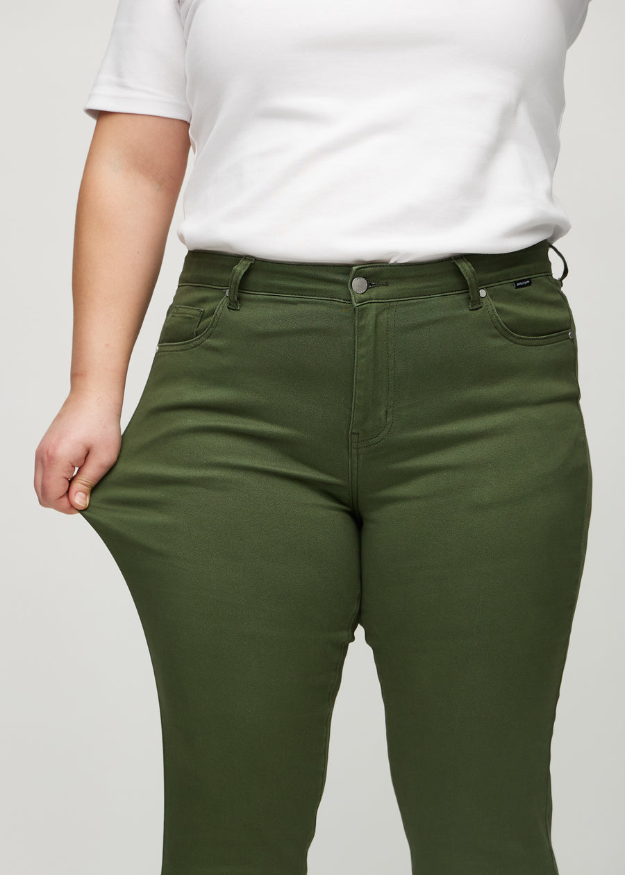 Slim jeans for women in dark green, color Renewals. A plus-size model stretches the jeans at the thigh to show the fabric&