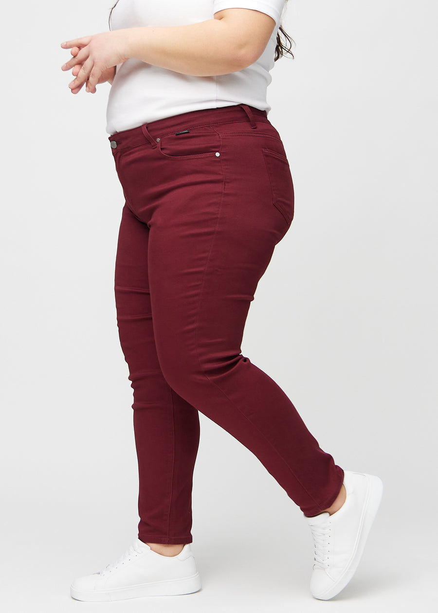 Slim jeans for women in dark red, color Santas. Side view on a plus-size model.