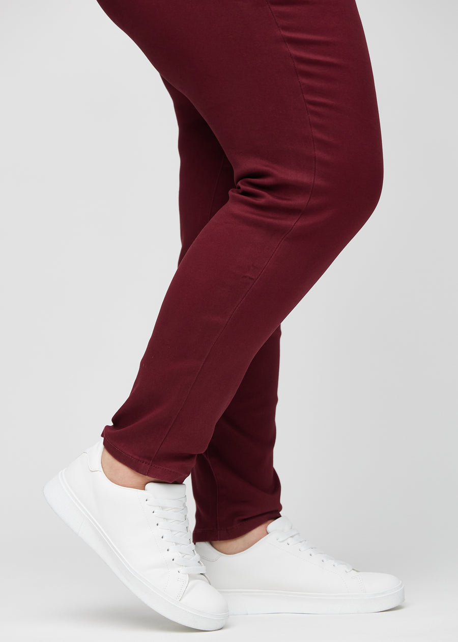 Slim jeans for women in dark red, color Santas. Close-up at the ankles on a plus-size model, showing the fit at the leg openings.