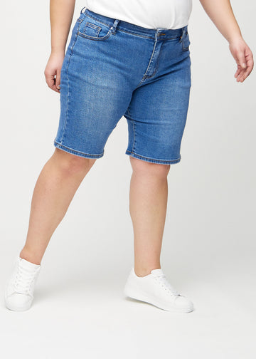 Denim regular middle shorts, model name Rivers, which fall straight down the leg and end just above the knee on a plus-size model, seen from the front.