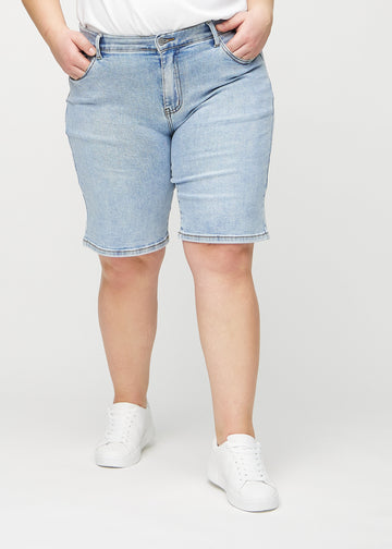 Light denim regular middle shorts, model name Waves, which go straight down the leg and end just above the knee on a plus-size model, seen from the front.