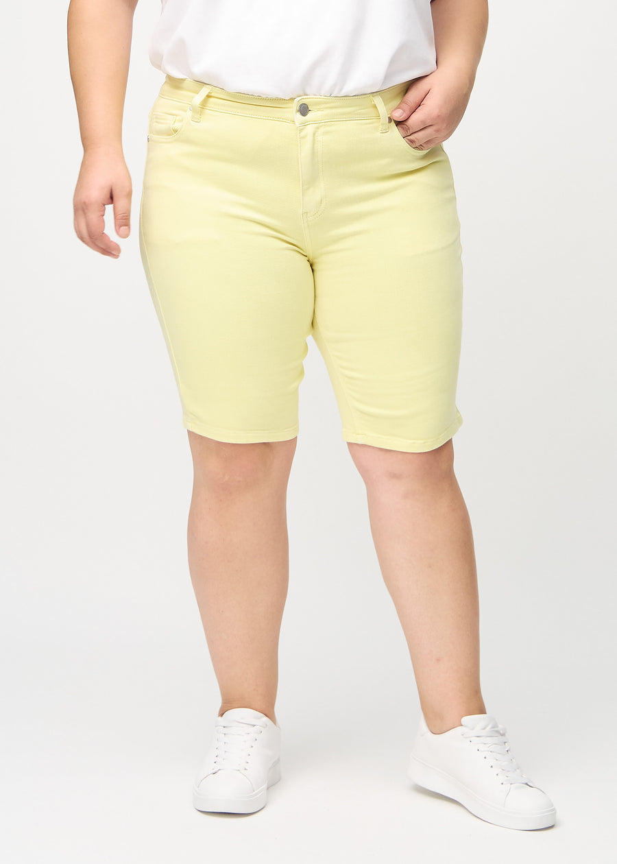 Light yellow skinny middle shorts, model name Lemonades, which fit tightly around the thigh and end just above the knee on a plus-size model, seen from the front.