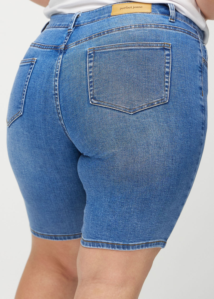 Denim skinny middle shorts seen from the back close up on a plus-size model to show details.