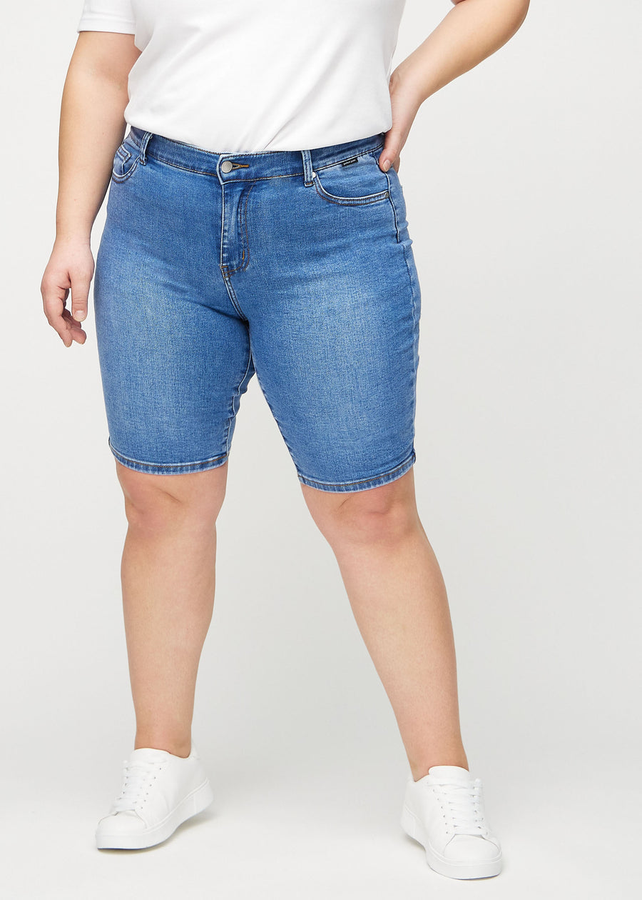 Denim skinny middle shorts, model name Rivers, which fit tightly around the thigh and end just above the knee on a plus-size model, seen from the front.
