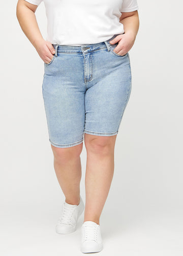 Light denim skinny middle shorts, model name Waves, which fit tightly around the thigh and end just above the knee on a plus-size model, seen from the front.