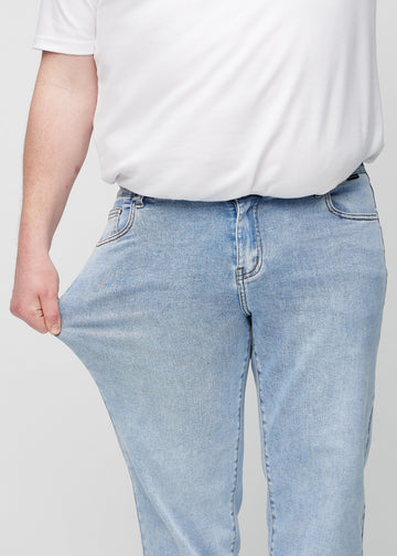 The plus-size model stretches the jeans at the thigh to show the stretch.